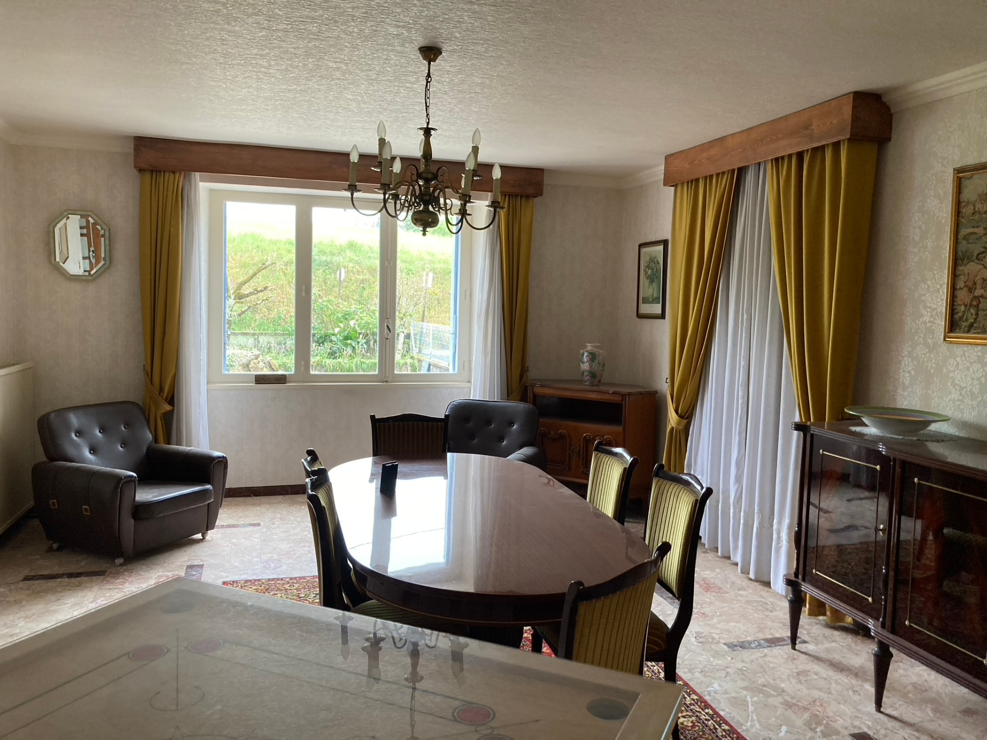 Avant travaux : séjour d'époque avec rideaux moutarde, lustre en laiton et mobilier ancien en bois verni — projet à Saint-Gilles-les-Hauts, Ouest de La Réunion