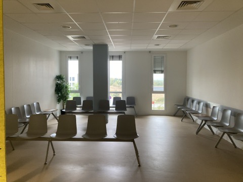 Avant travaux : grande salle d'attente avec rangées de chaises grises, poteau central et fenêtres hautes — secrétariat médical à Toulouse