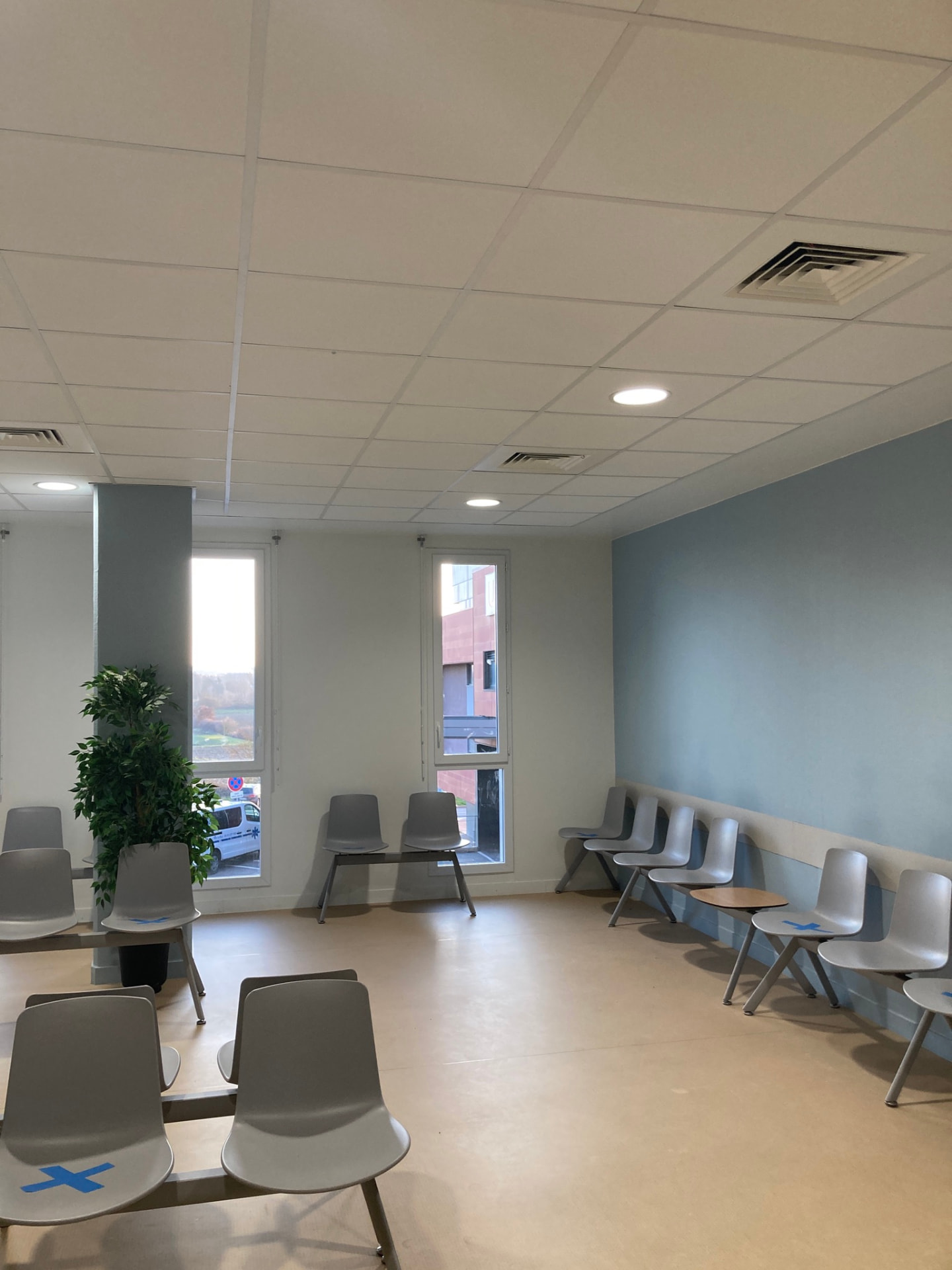 Avant travaux : salle d'attente avec chaises grises alignées, mur bleu et faux plafond — secrétariat médical à Toulouse