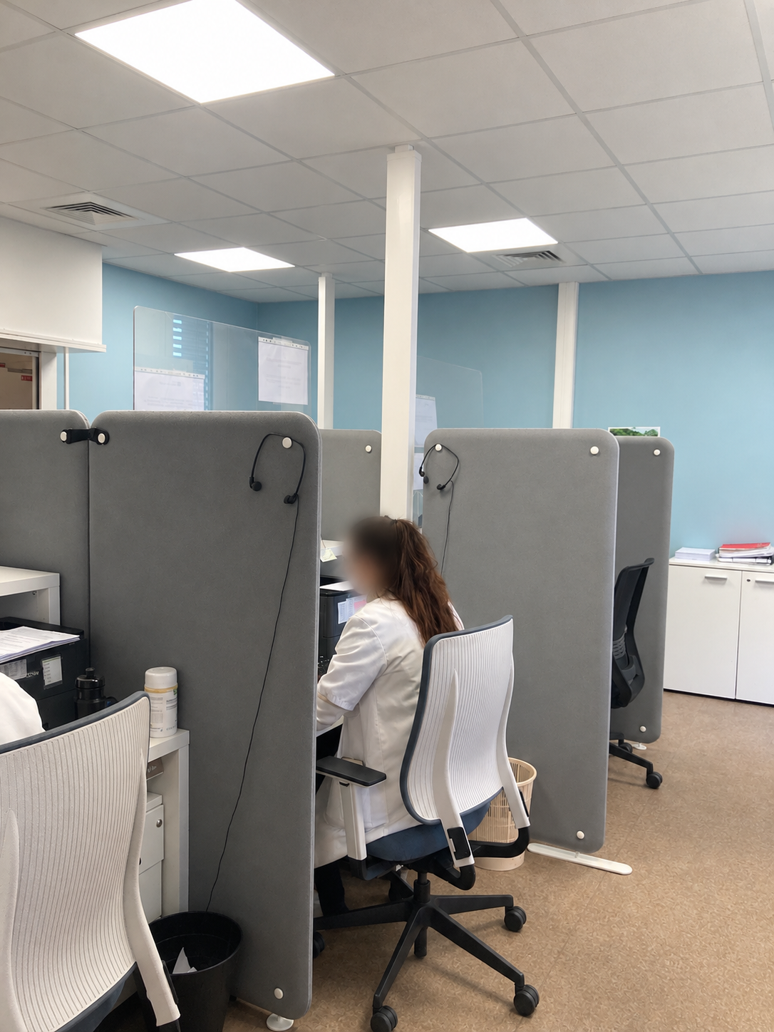 Avant travaux : postes de travail séparés par des cloisons grises mobiles, murs bleus et faux plafond — secrétariat médical à Toulouse